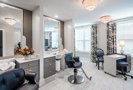 Longleaf salon stylist stations at left with blue and chrome client chairs, white sinks and mirrors and a white manicurist table and blue chairs at rightby windows