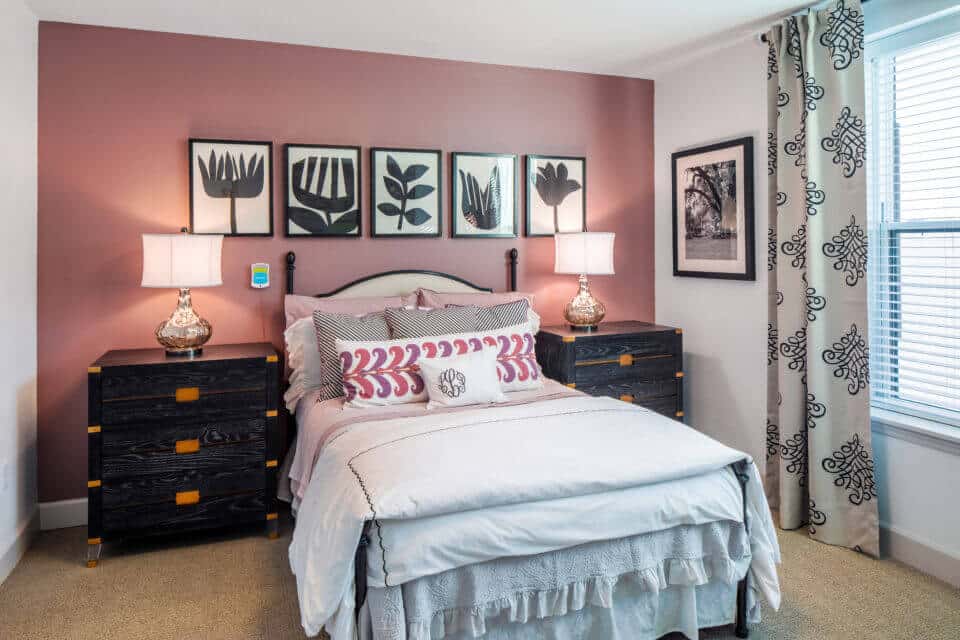 White bed with colorful pillow, black nightstands, black and white framed art, glass lamps with white shades in Longleaf assisted living model apartment