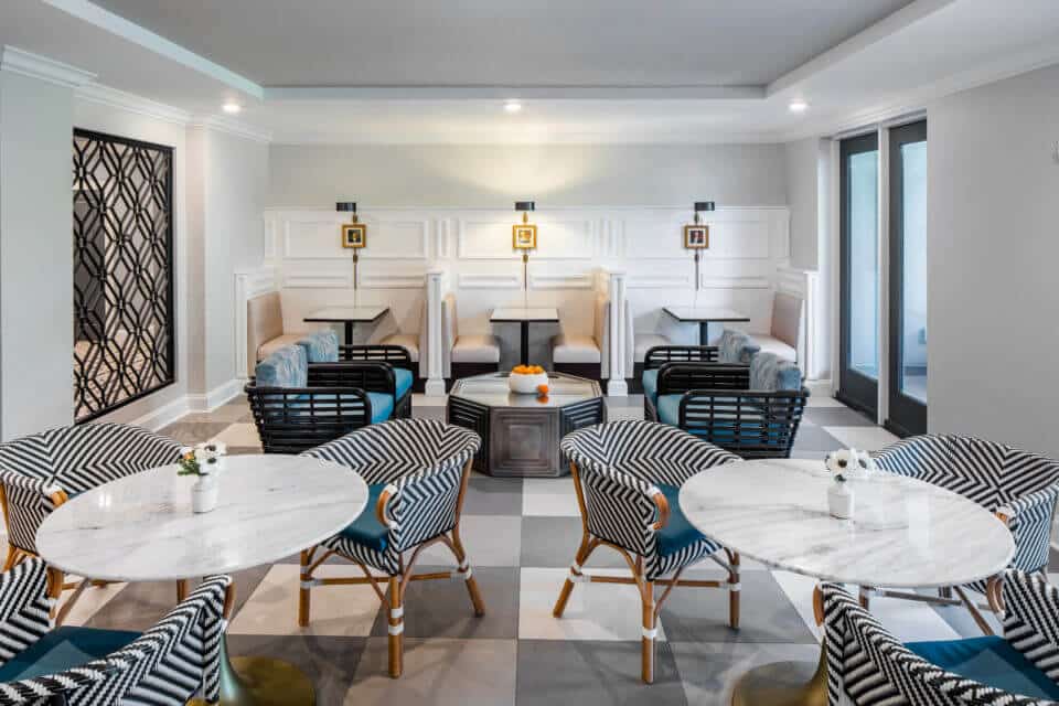 Two white tables with black and white chairs, four blue chairs and table, and three booths at back of Longleaf bistro