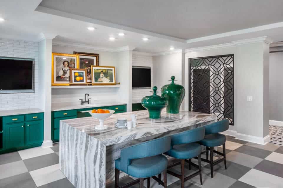 Breakfast bar with three blue chairs, checkered floor and green cabinets and white walls with framed art and TVs at back of Longleaf Bistro