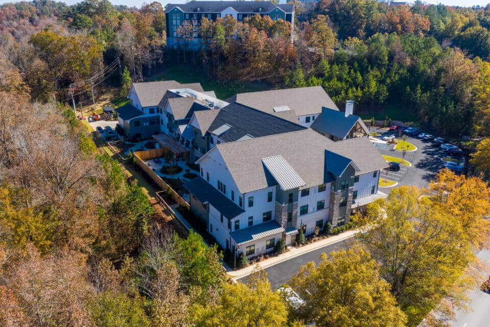 Aerial view of Longleaf community looking at left side of community with fenced memory care patios in view and front entrance to the right and fall trees surrounding community