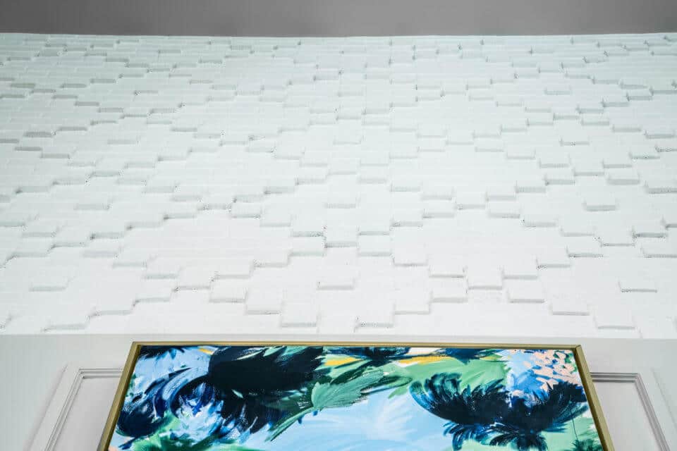 Close up view looking up at white textured wall with partial view of blue, green and yellow framed art in Longleaf foyer