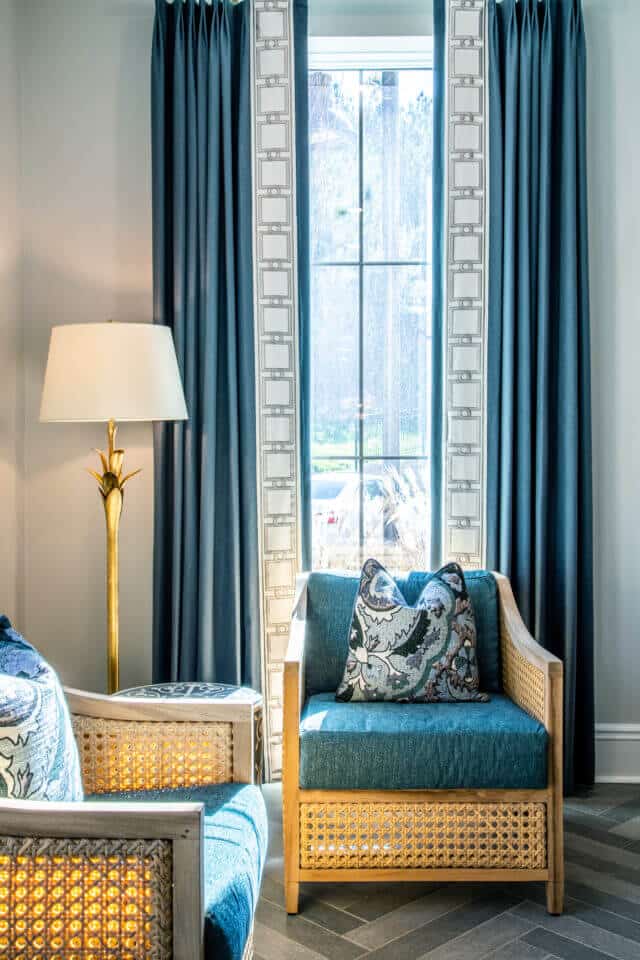 Two tan wicker chairs with blue cushions in front of window with blue curtains and a white and gold lamp at left in Longleaf common space