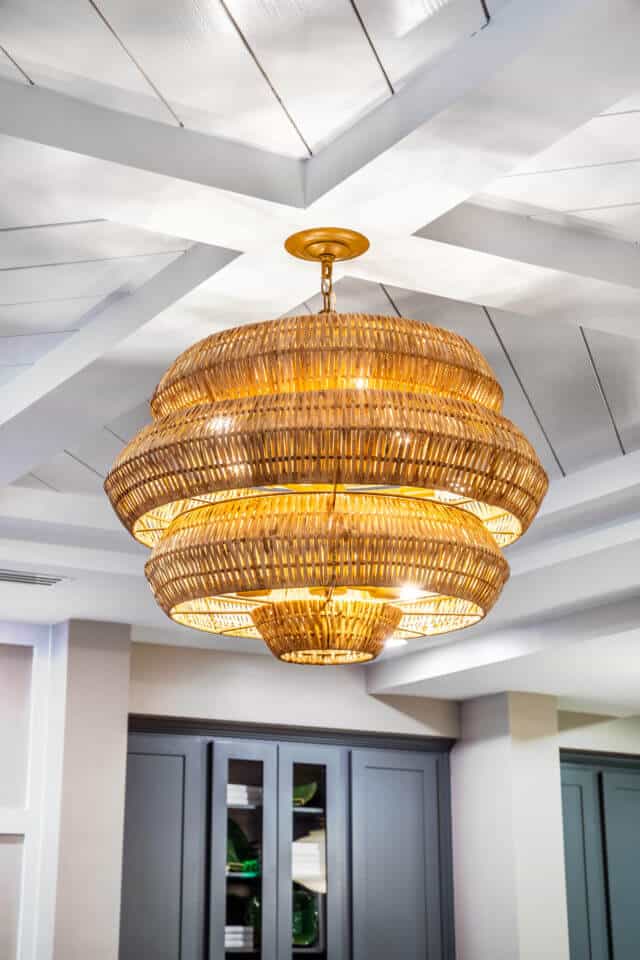 Basket weave like light fixture hanging from white wooden ceiling in Longleaf common space with blue cabinets at back