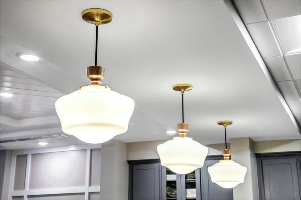 White and gold light fixtures hanging from white ceiling in Longleaf common space