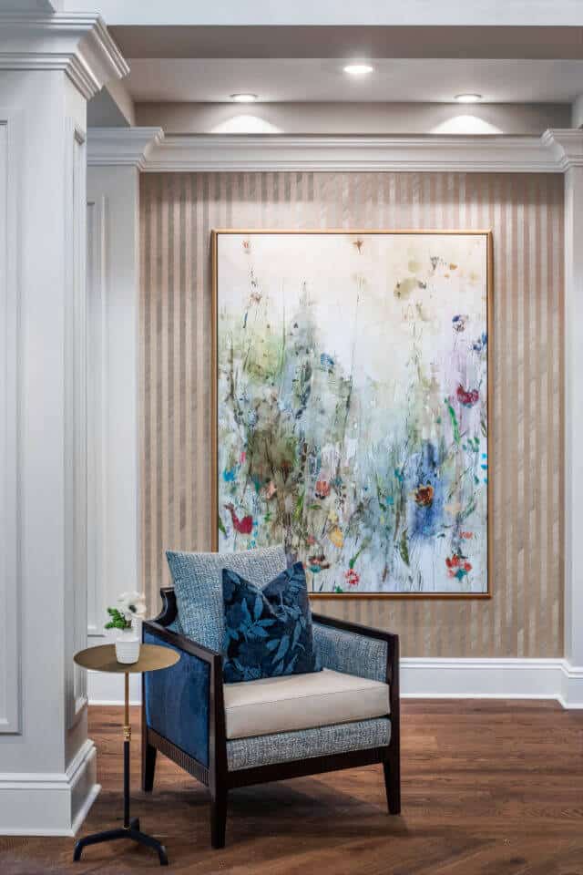 Longleaf common space with blue and tan chair, gold table, flowers in white vase, floral painting on wall behind