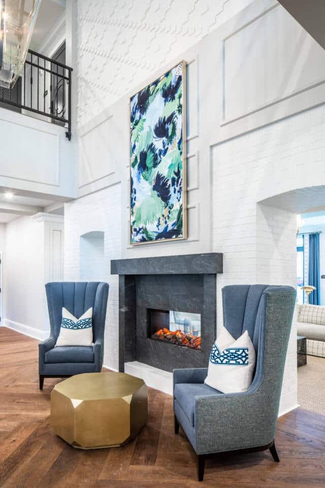 Longleaf foyer with gray see-through fireplace, blue chairs, gold table and blue/green painting on white wall