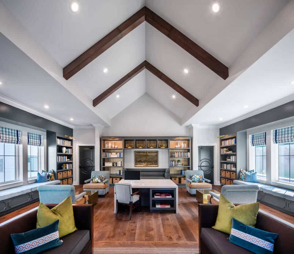 Longleaf library windows at left and right next to gray bookcases with desk in center, chairs and couches throughout room