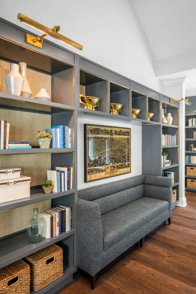 Longleaf library with gray shelves filled with books, gold and white decor, wicker baskets and gray sofa