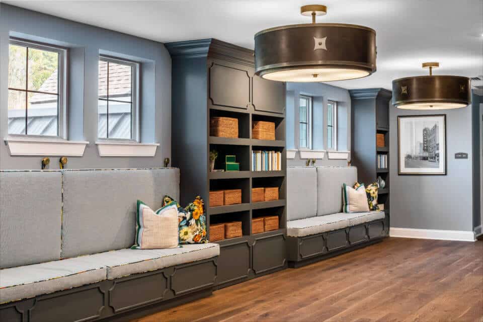 Longleaf common space with bench seating and pillows under windows, gray wood bookcases and paneling with large round light fixtures hanging from ceiling