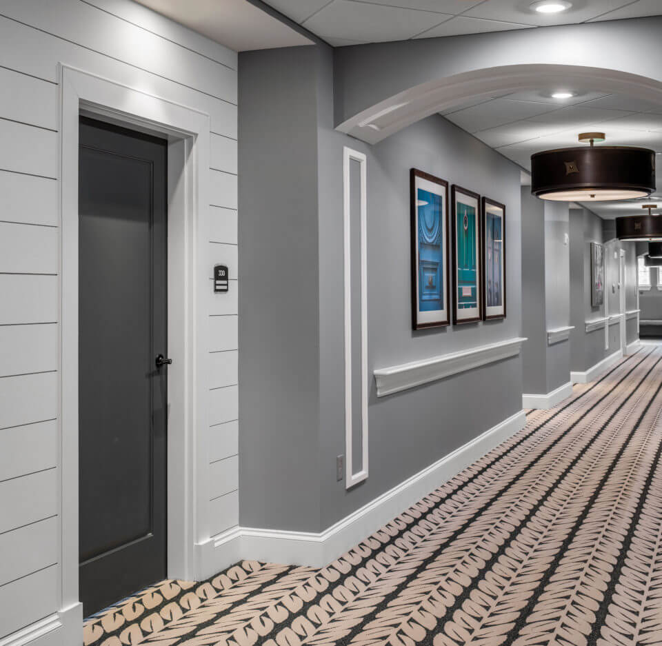Longleaf hallway with white walls and residents' blue doors at left, gray walls to right of door
