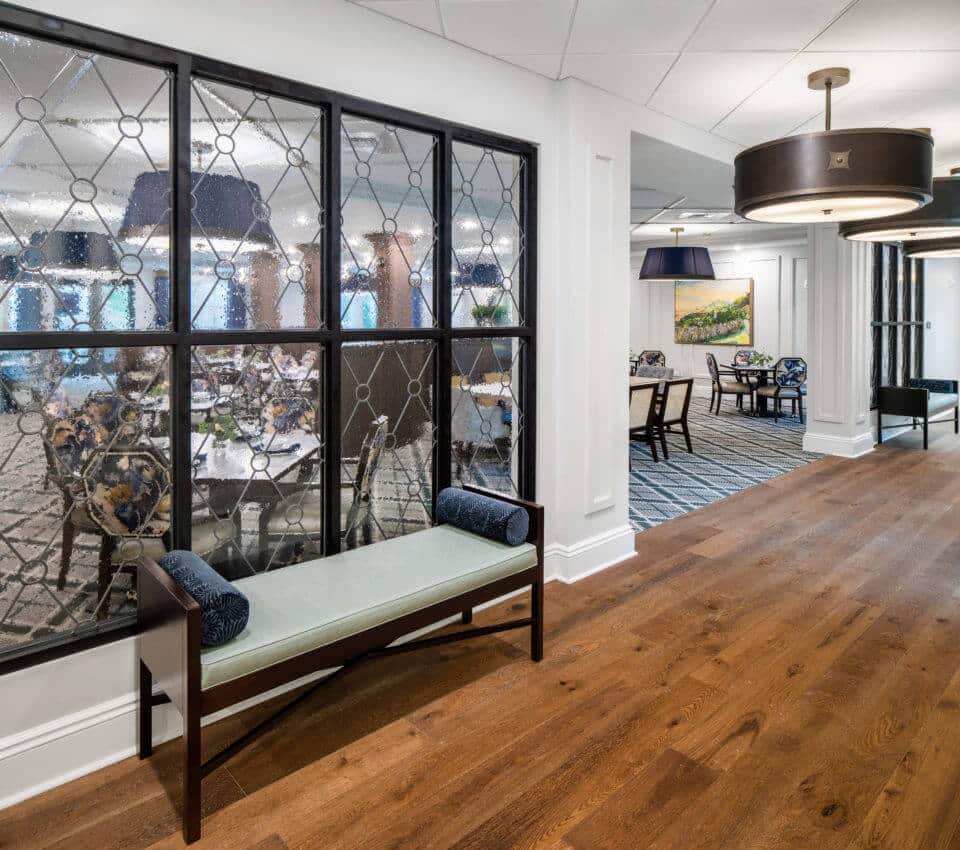 Longleaf hallway at right, bubble glass window at left looking into main dining room with bench and pillows below