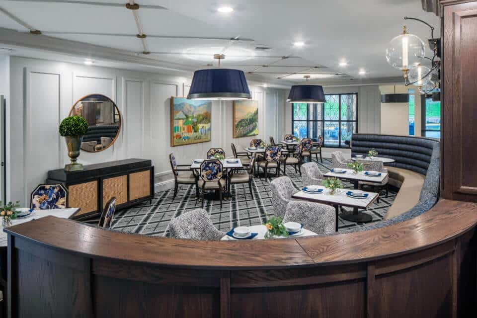 Longleaf main dining room blue and beige curved booth, tables and chairs with wood columns and globe light fixtures at right, buffet table, mirror and potted plant at left