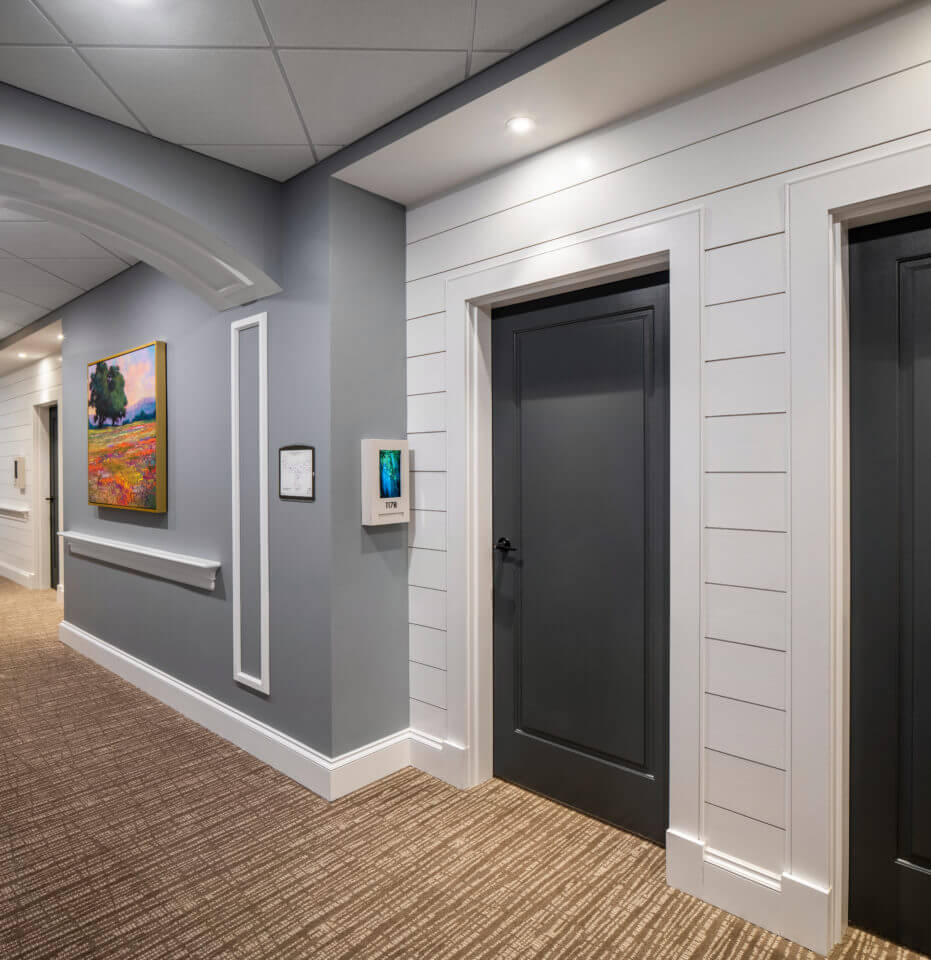 Longleaf hallway with white walls and residents' blue doors at right, gray walls at left