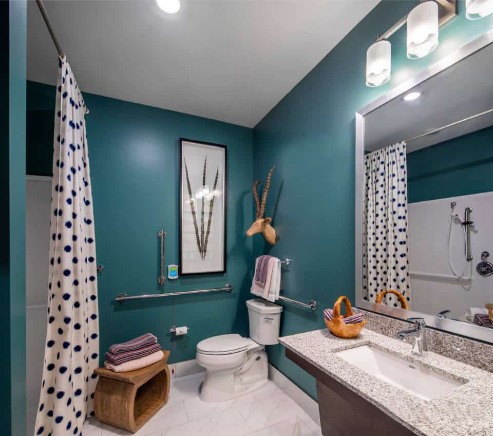 Teal bathroom with white polka dot curtains, granite vanity with sink in Longleaf memory care model apartment
