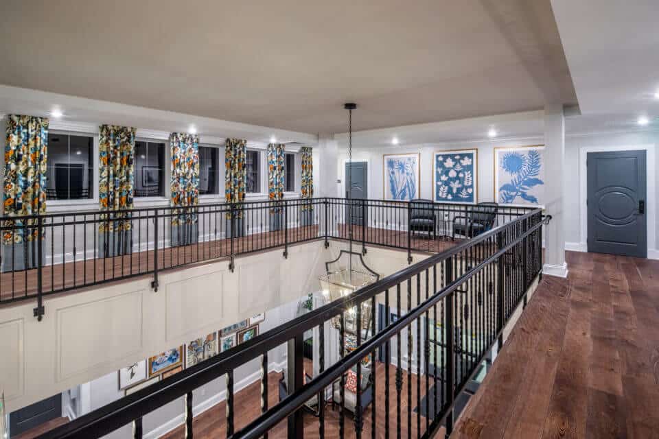 Longleaf second floor atrium with black railing, looking at windows with floral curtains to left, blue doors and paintings to right and first floor foyer below