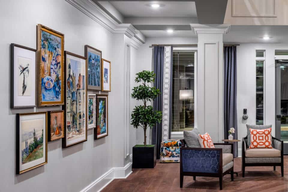 Framed art on wall to left, potted plant in corner and two chairs with table and flowers in vase in Longleaf common space