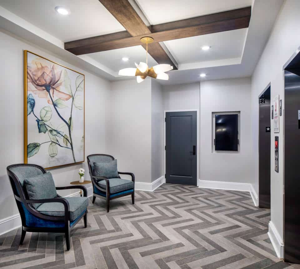 Longleaf common space with elevators at right and sitting area with two chair, table and painting at left