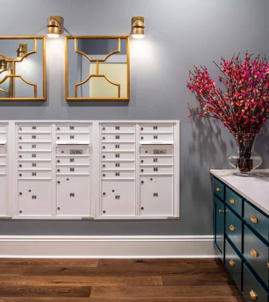 White mailboxes built into grey wall with gold mirrors and light fixtures above mailroom at Longleaf