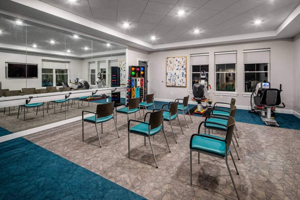 Longleaf fitness room with chairs in rows and wall of mirrors with ballet bar and exercise equipment at right