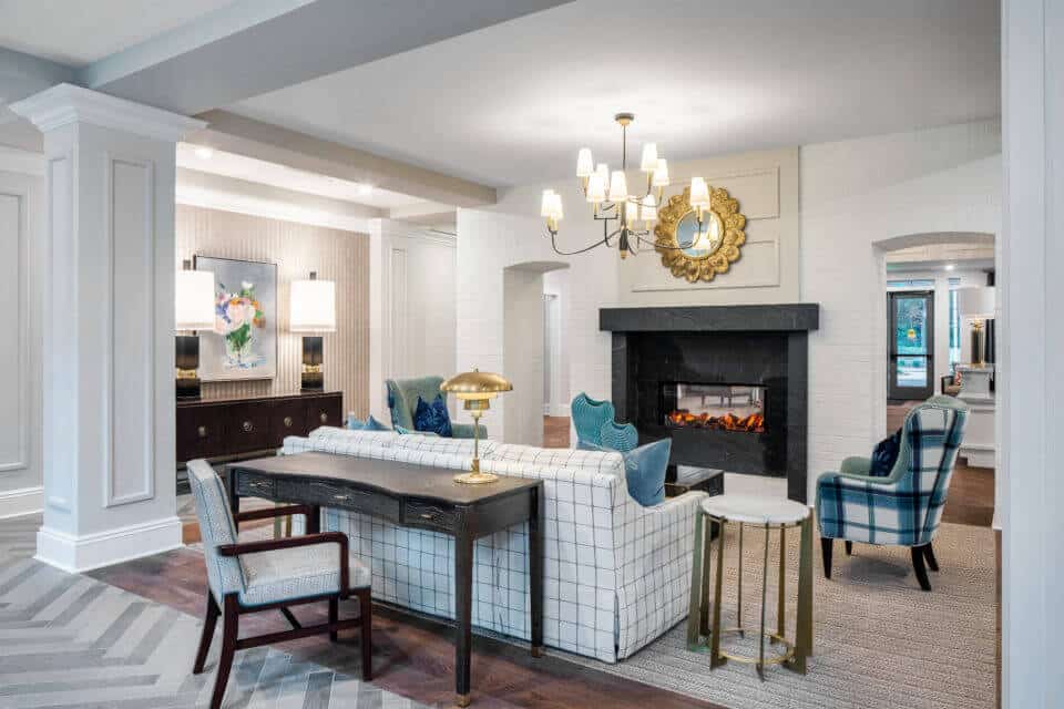 Black desk, gray chair behind a white plaid sofa, black ottoman, blue plaid chairs in front of fireplace in Longleaf common area